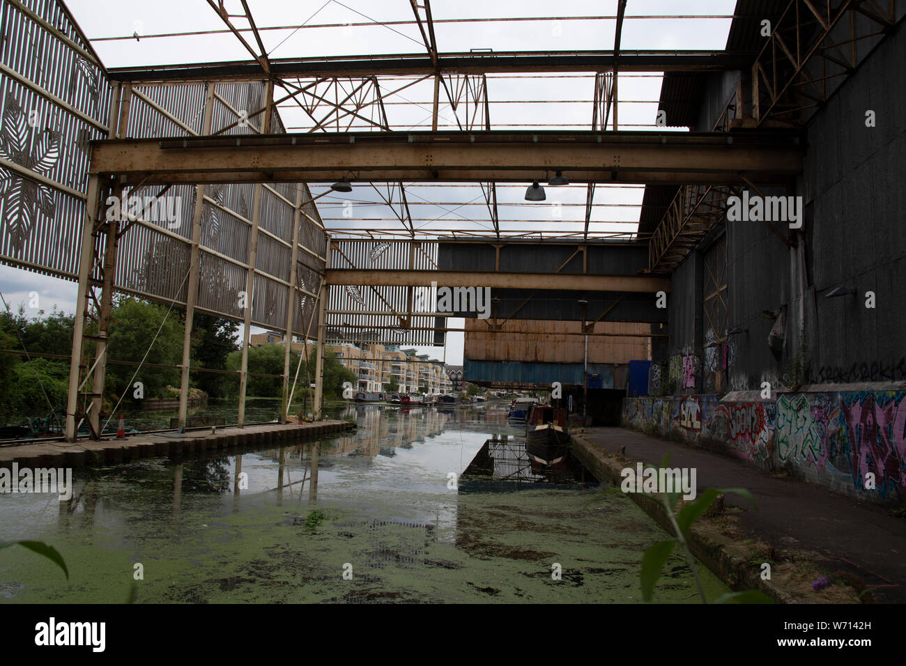 A derelict warehouse on the Grand Union Canal with new developments of flats and apartment blocks in the background, Brentford, London, Middlesex UK Stock Photo
