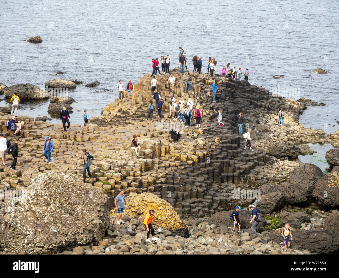 County Antrim, Northern Ireland, UK – July 17, 2019: Visitors on Giant’s Causeway, unique hexagonal geological formation of volcanic basalt rocks. Stock Photo