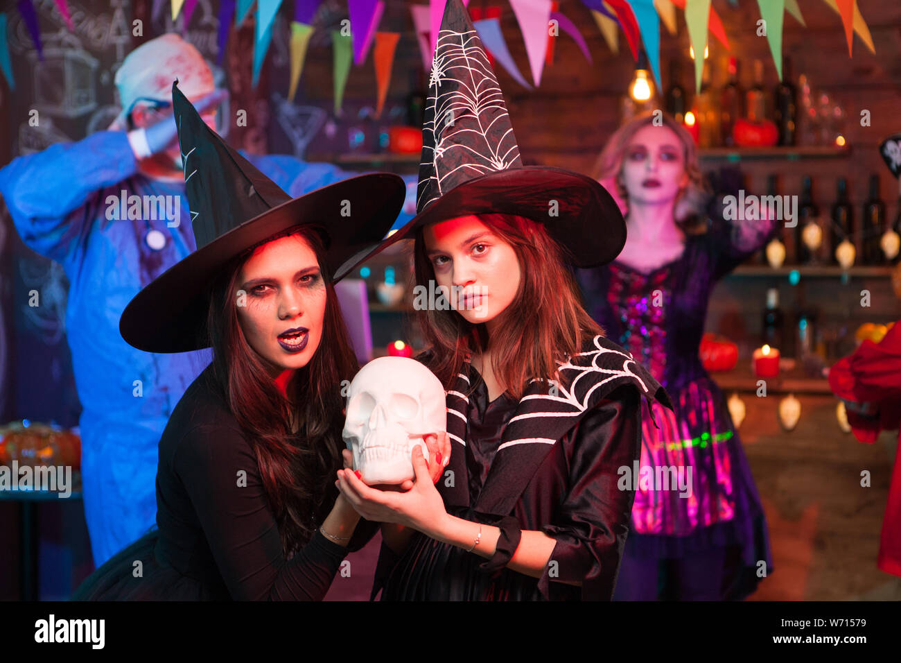 Witches with serious face holding a human skull at halloween