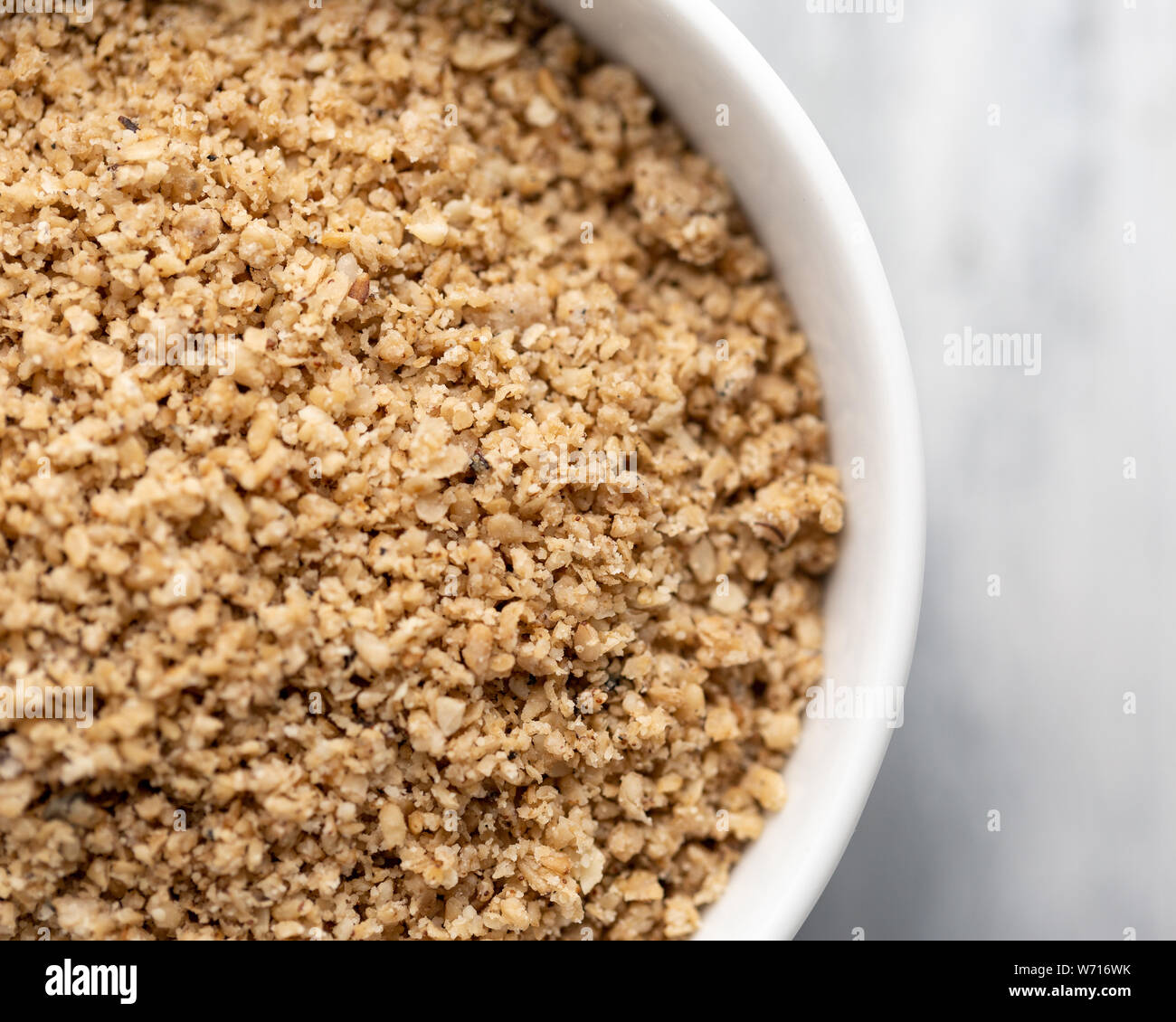 Finely ground egusi melon seeds in a white bowl, off centre to the left