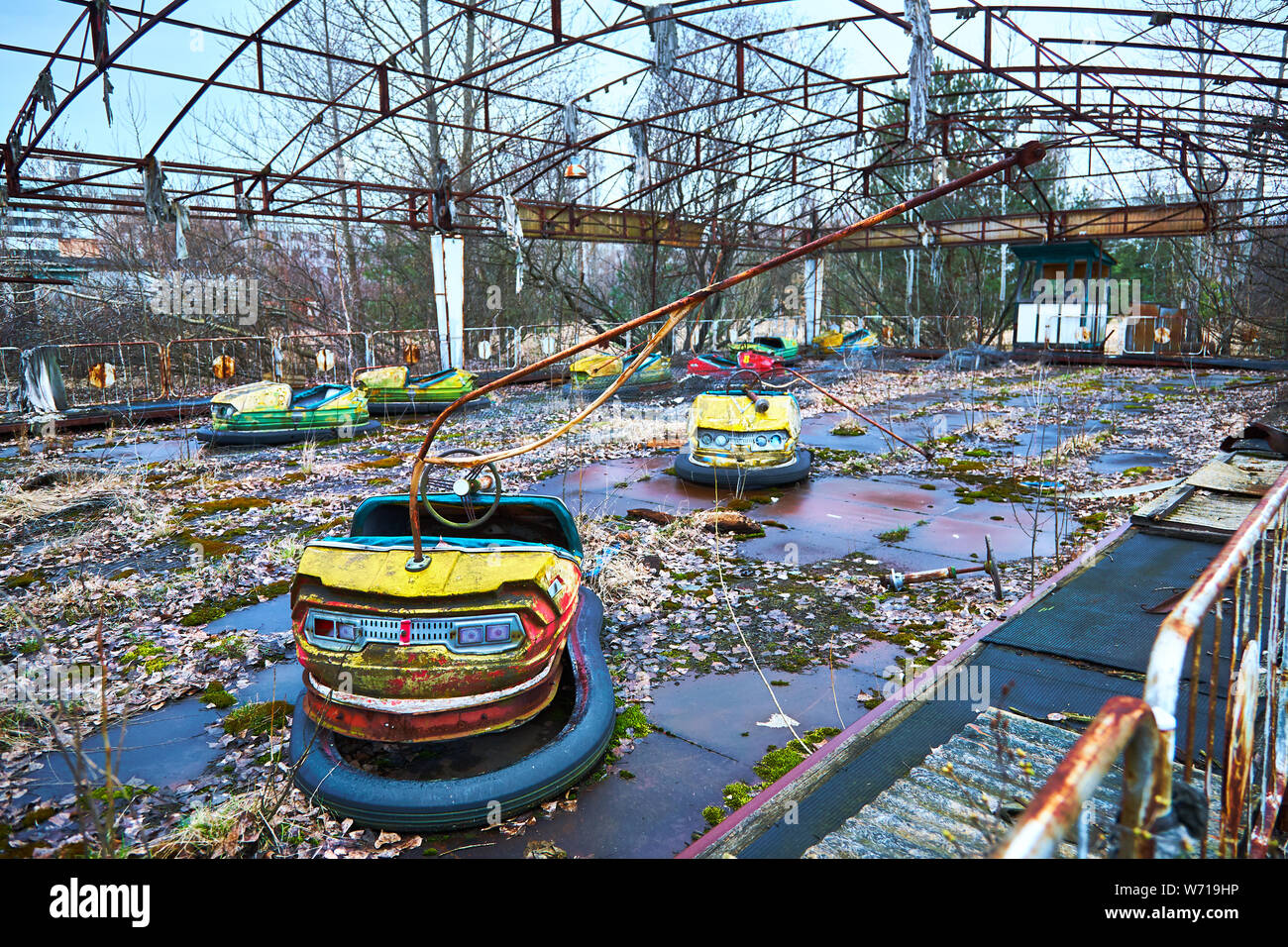 Old broken rusty metal radioactive yellow cars, childrens electric cars, abandoned among vegetation, the park of culture and recreation in the city of Stock Photo