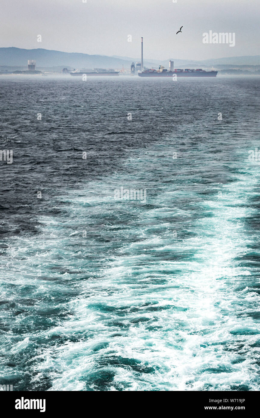 Views of the sea and the coast from a boat during cold and cloudy day. The ship moves away from the coast, beautiful views of the mountains and ocean. Stock Photo