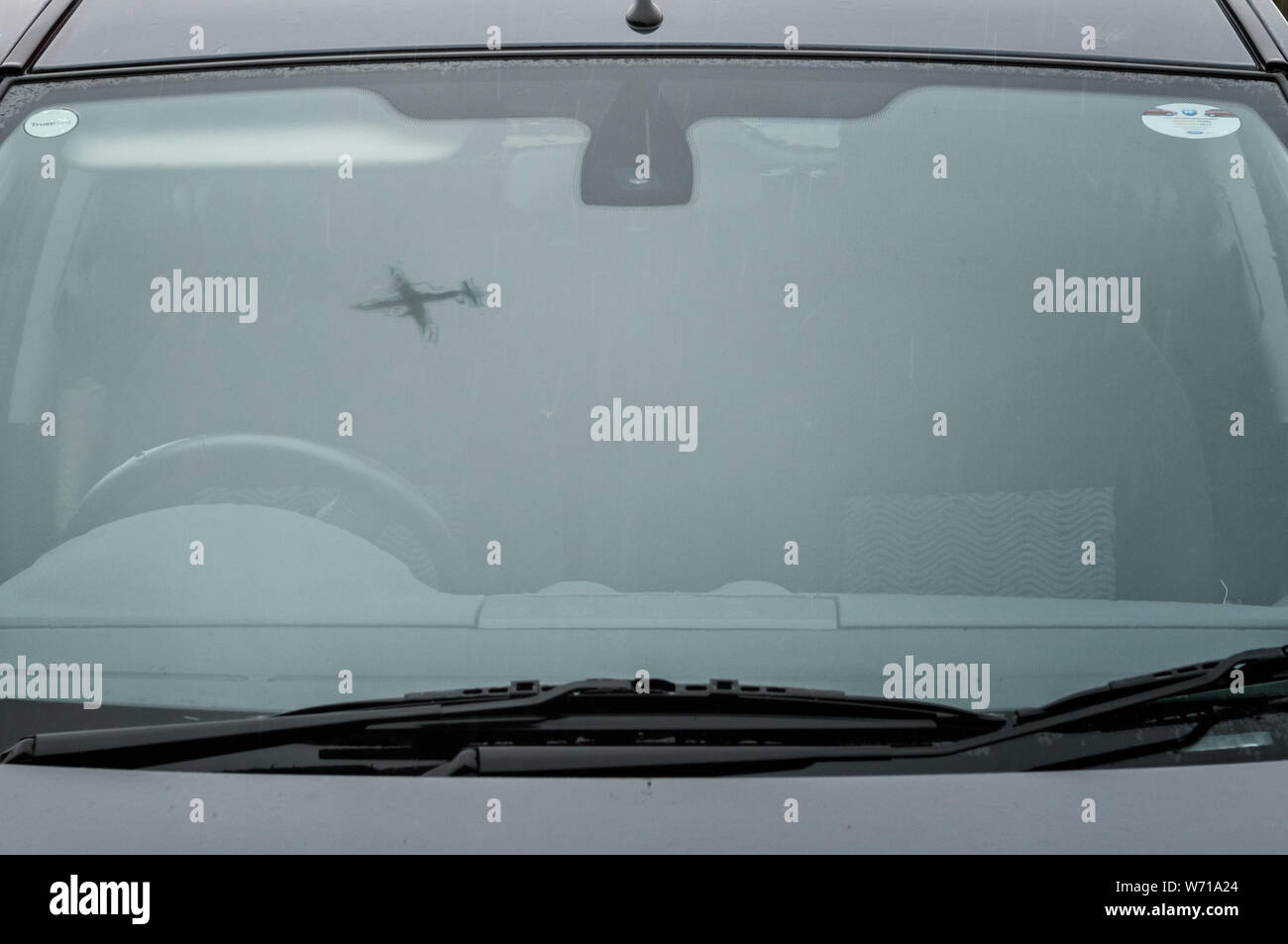 Flying airplane reflected in car windscreen, distorted by rain on the glass. Stock Photo