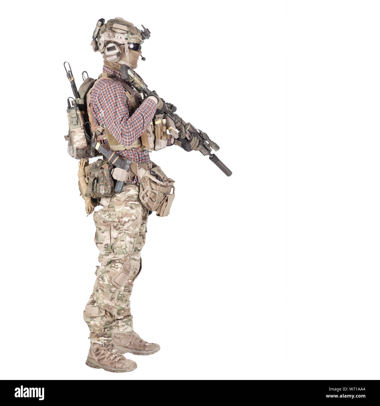 Full length portrait of airsoft player in checkered shirt, wearing camouflage uniform, helmet with tactical radio headset, body armour, aiming with service rifle replica studio shoot isolated on white Stock Photo