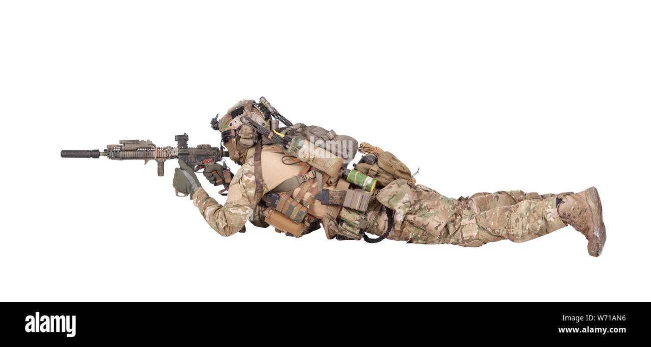 Modern army soldier, infantry rifleman equipped with tactical ammunition and radio, lying on ground, observing territory trough optical sight, aiming, shooting with assault rifle isolated studio shoot Stock Photo