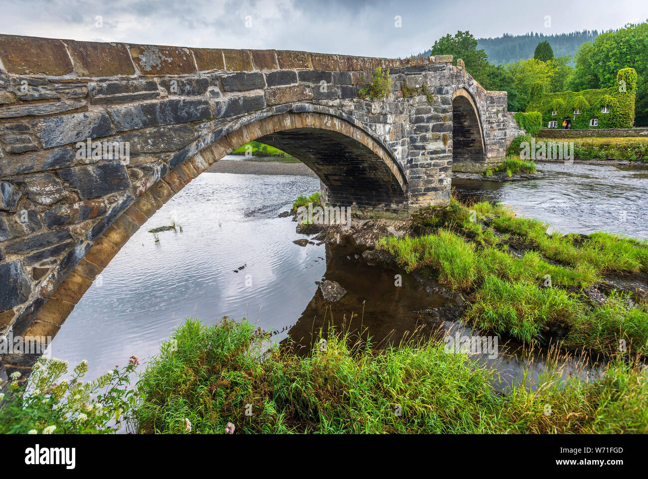 Stone roadbridge over the river Conwy at Llanrwst with the Virgina creeper covered tearoom in the background. Stock Photo