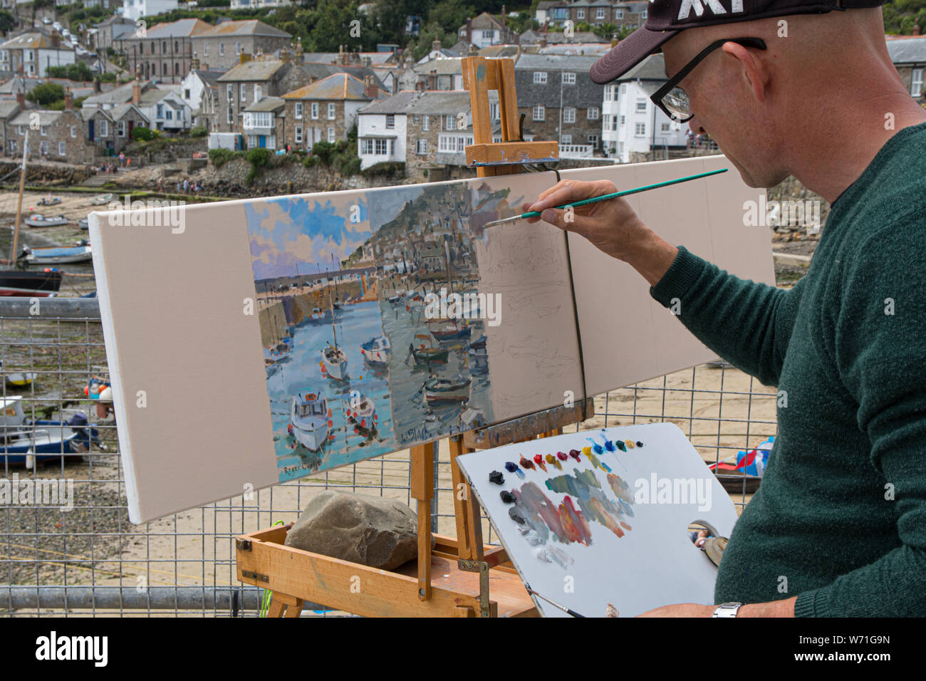 Mousehole, Cornwall, UK. 4th August 2019. Seen here Tim Hall, a former winner of the Sea Pictures Gallery Award by Royal society of Marine Artists, painting his section of a panorama of Mousehole harbour and village. the picture will be auctioned off later to raise funds for the annual festival. The other artists painting are Roger Curtis, Lizzie Black, Tom Rickman, Jeremy Sanders, Judy Joel and finally Nigel Hallard. Credit Simon Maycock / Alamy Live News. Stock Photo