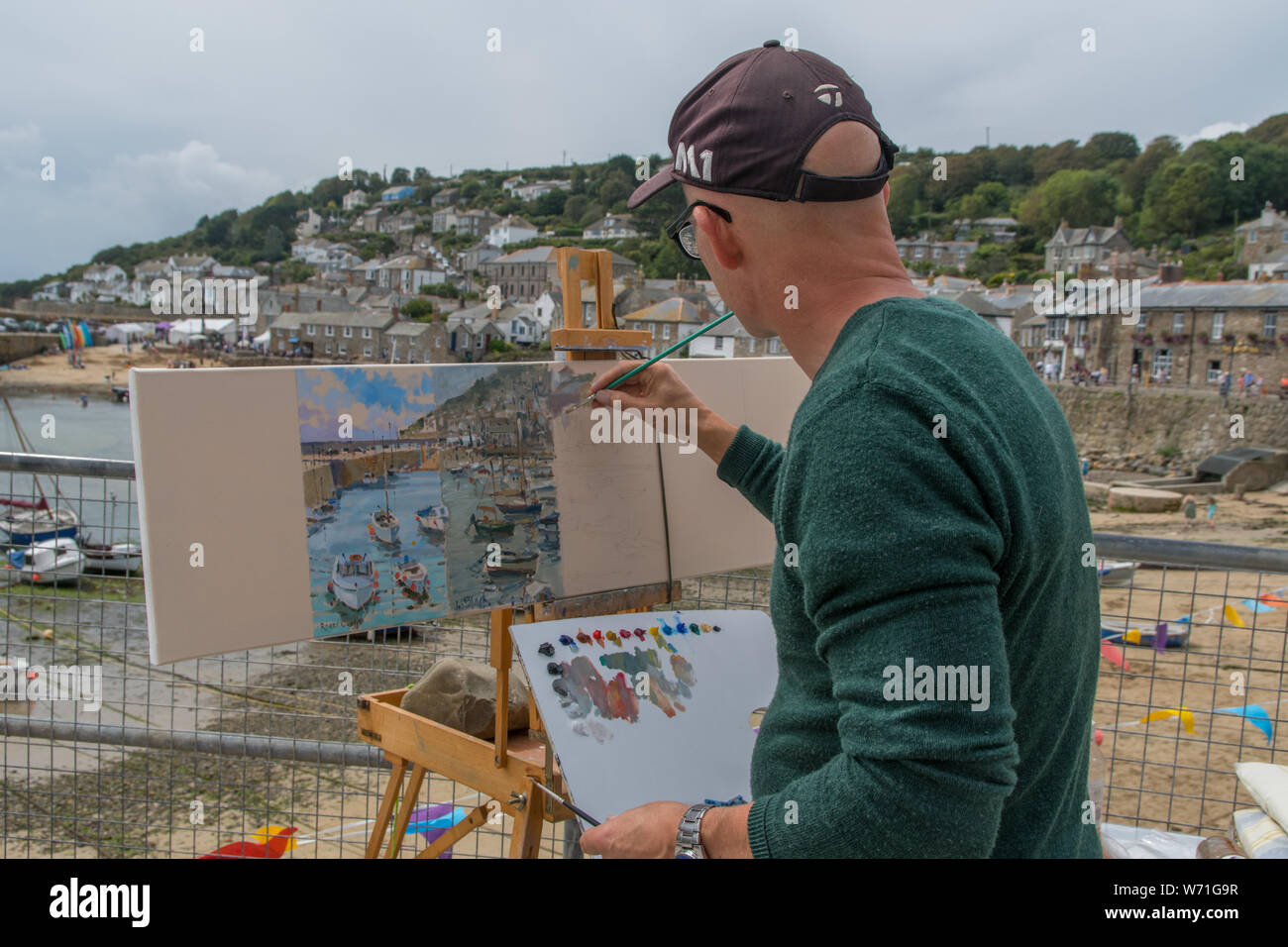 Mousehole, Cornwall, UK. 4th August 2019. Seen here Tim Hall, a former winner of the Sea Pictures Gallery Award by Royal society of Marine Artists, painting his section of a panorama of Mousehole harbour and village. the picture will be auctioned off later to raise funds for the annual festival. The other artists painting are Roger Curtis, Lizzie Black, Tom Rickman, Jeremy Sanders, Judy Joel and finally Nigel Hallard. Credit Simon Maycock / Alamy Live News. Stock Photo