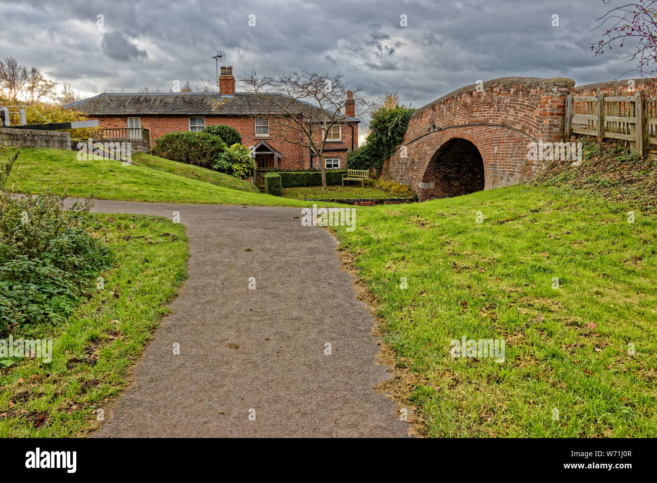 A small brick bridge over Grantham Canal with a house to the side of it and stormy clouds overhead Stock Photo