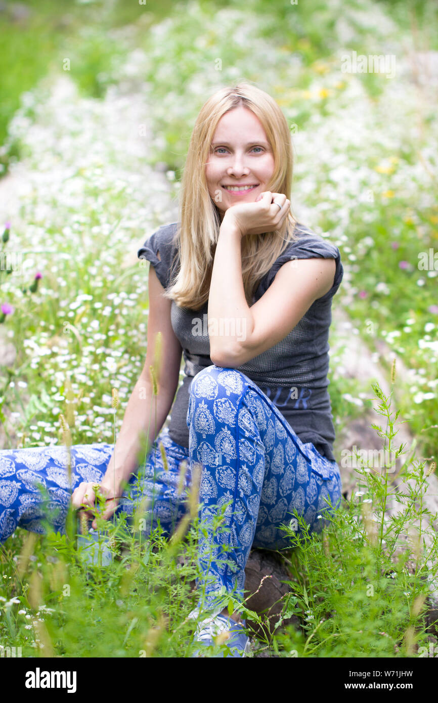 blonde woman sitting on meadow with white flowers Stock Photo