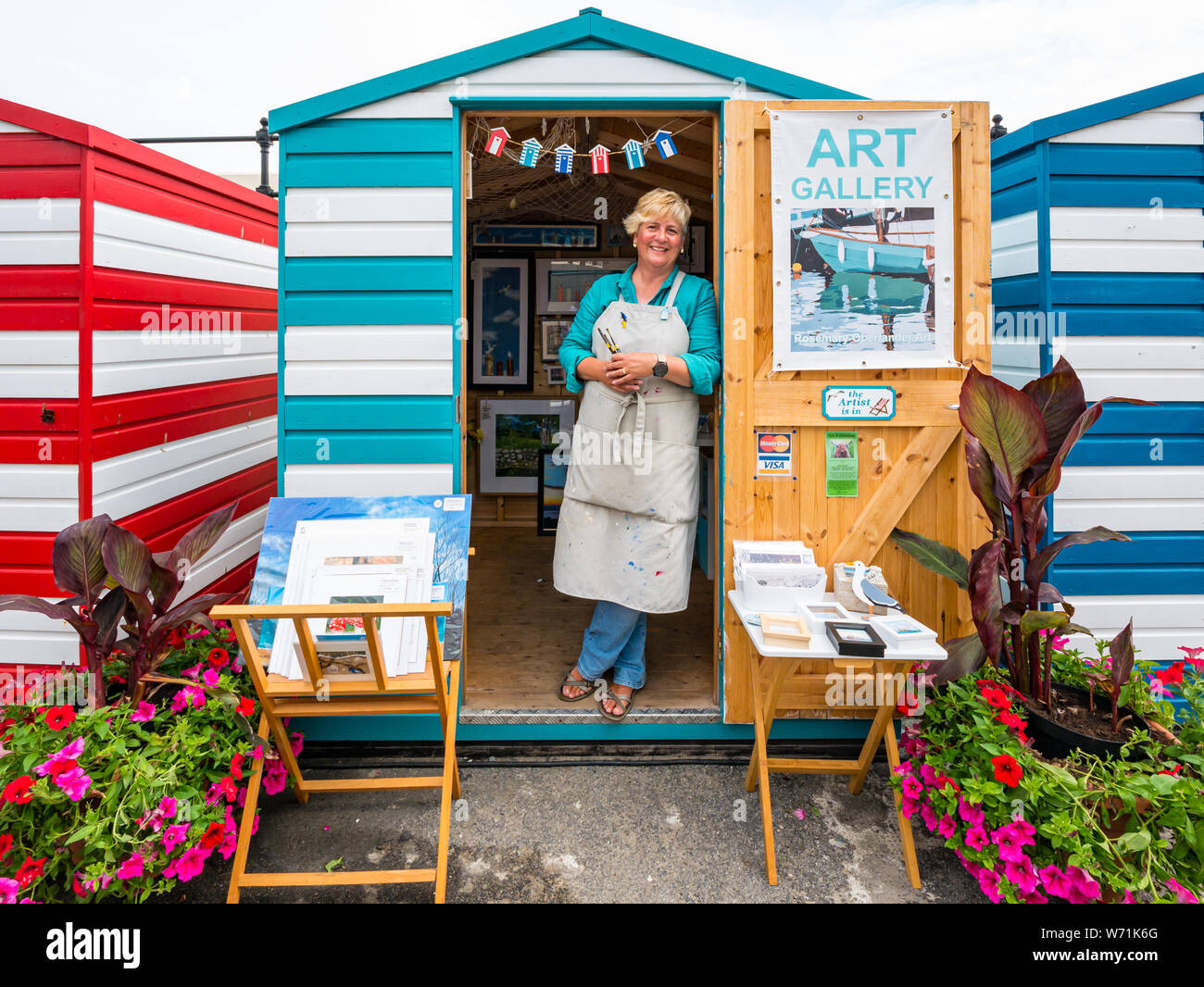 North Berwick, East Lothian, Scotland, UK, 4th August 2019. A local artist in the colourful beach huts in the harbour area. Pictured: artist painter Rosemary Oberlander Stock Photo