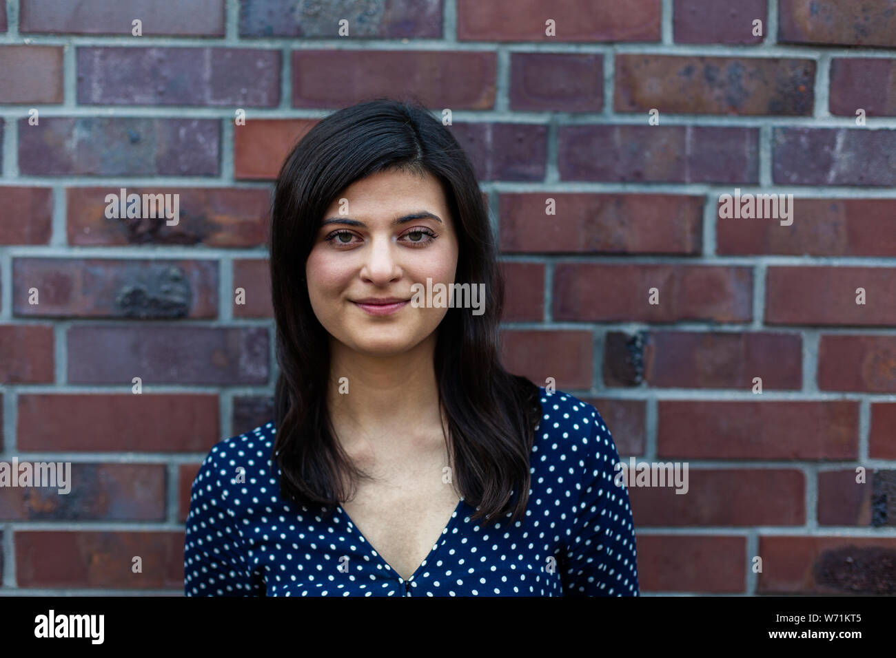 Cheerful young woman smiling at camera while standing in front of brick ...