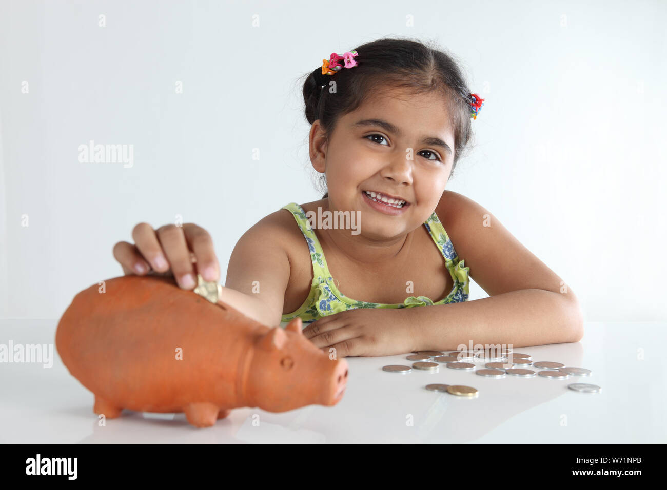 Girl inserting coin into a piggy bank and smiling Stock Photo - Alamy