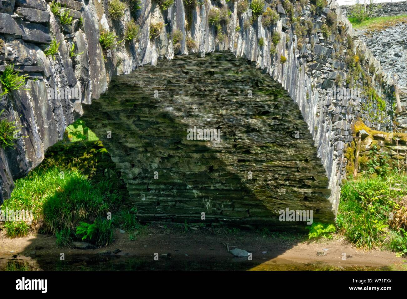 English dry stone arch formed of square and rectangular profile stones over river with reflection of water on underside of bridge Stock Photo