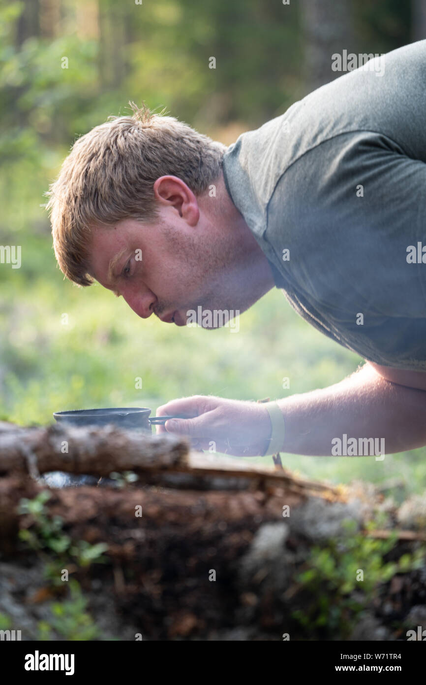 A man blowing on a camp fire in a forest to start the fire Stock Photo