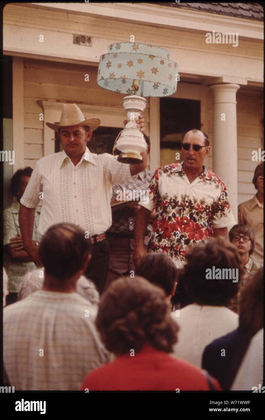 AN AUCTIONEER'S HELPER HOLDS A LAMP UP AS THE AUCTIONEER ASKS FOR BIDDING ON IT AT AN AUCTION IN NEW ULM, MINNESOTA. THEY USUALLY ARE HELD IN THE SUMMER MONTHS TO SELL HOUSEHOLD POSSESSIONS OF PEOPLE WHO ARE MOVING TO APARTMENTS, OR WHO HAVE DIED. NEW ULM IS A COUNTY SEAT TRADING CENTER OF 13,000 IN A FARMING AREA OF SOUTH CENTRAL MINNESOTA. IT WAS FOUNDED IN 1854 BY A GERMAN IMMIGRANT LAND COMPANY THAT ENCOURAGED ITS KINSMEN TO EMIGRATE FROM EUROPE Stock Photo