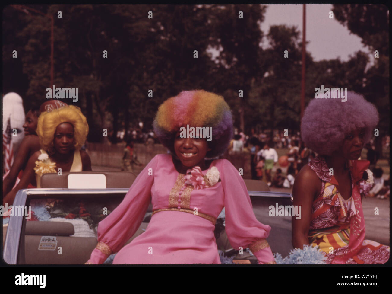 BLACK BEAUTIES WITH COLORFUL HAIR GRACE A FLOAT DURING THE ANNUAL BUD BILLIKEN DAY PARADE ALONG DR. MARTIN L. KING JR. DRIVE ON CHICAGO'S SOUTH SIDE. UP TO HALF A MILLION PEOPLE VIEW ONE OF THE LARGEST EVENTS OF THE YEAR, HELD FOR BLACKS OF ALL AGES AND ECONOMIC STATUS. THE PARADE ALSO INCLUDES BLACK POLITICIANS, BLACK BUSINESSES DISPLAYING THEIR PRODUCTS AND BLACK BANDS; General notes:  Women in wigs ride on car in the Bud Billiken Parade, Chicago, 1973. Stock Photo