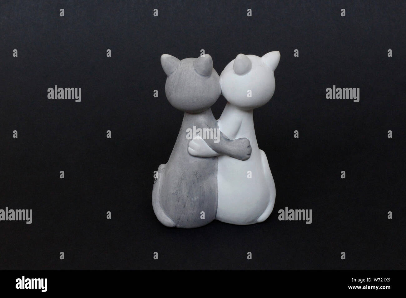 Love - hugging cats. Toy, figurine - white and gray cats are standing in an embrace. Black background. Together with a cat. Friendship and trust. Stock Photo