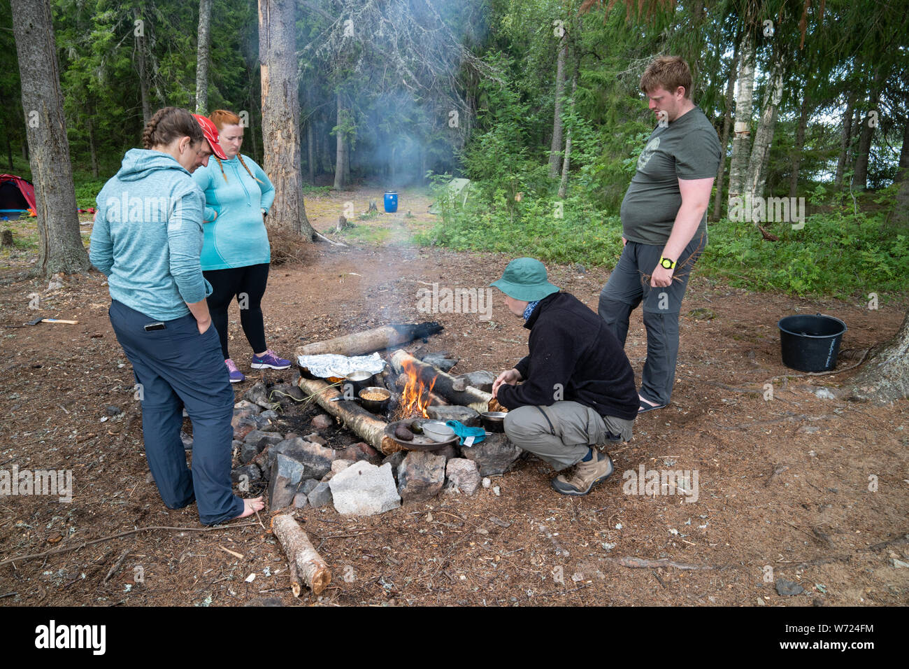 Friends wild camping in a forest. Four people around a camp fire. Stock Photo