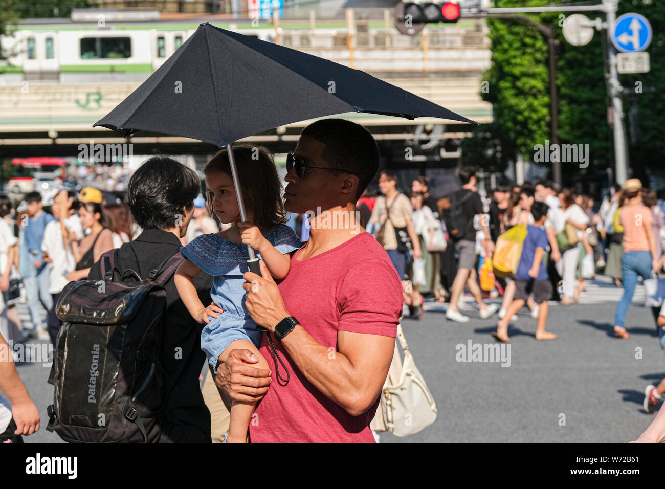 A man carrying his kid holds an umbrella at the Shibuya crossing in ...