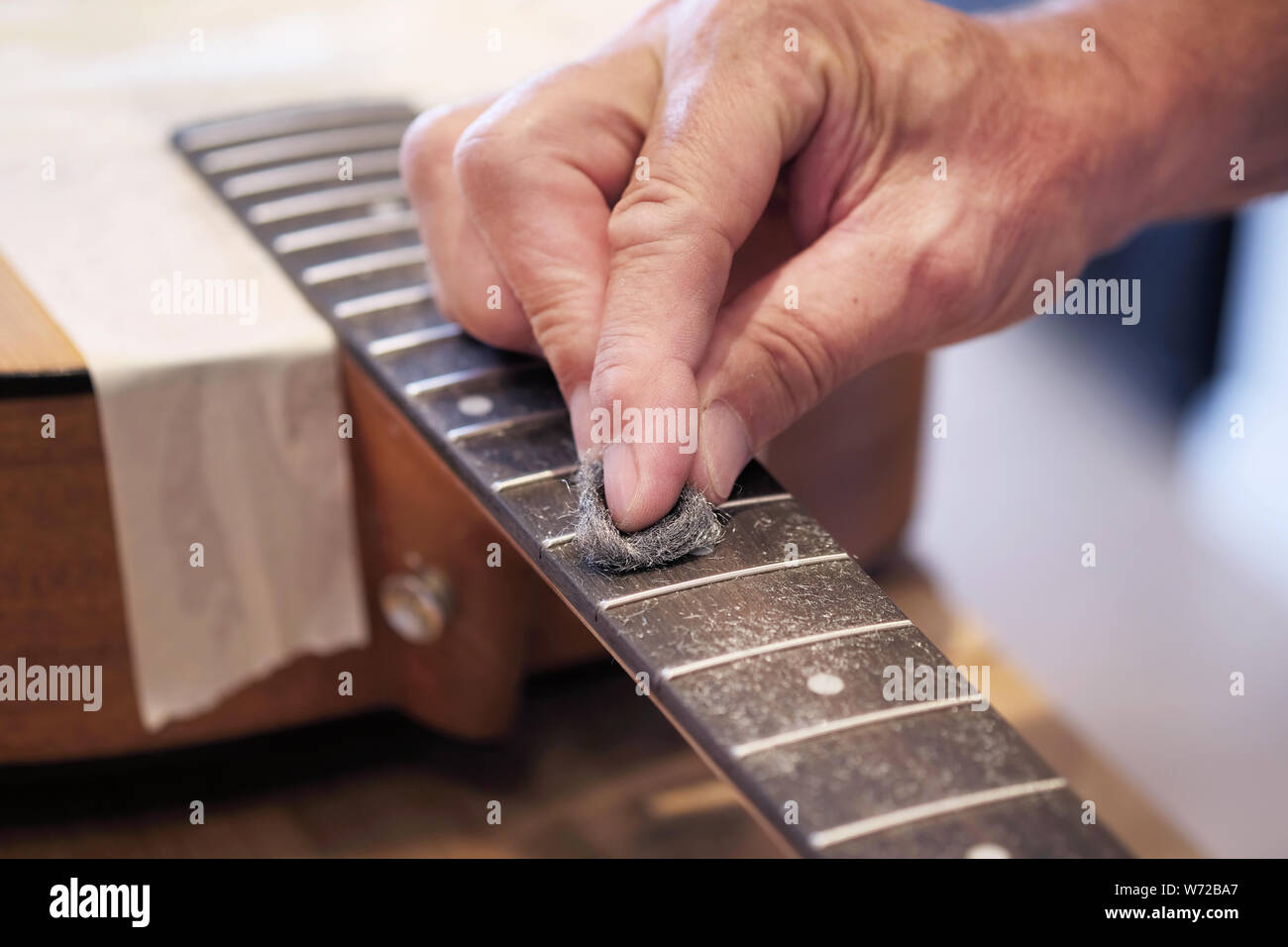 An acoustic guitar being serviced. The technician is Cleaning the fret board with fine wire wool Stock Photo