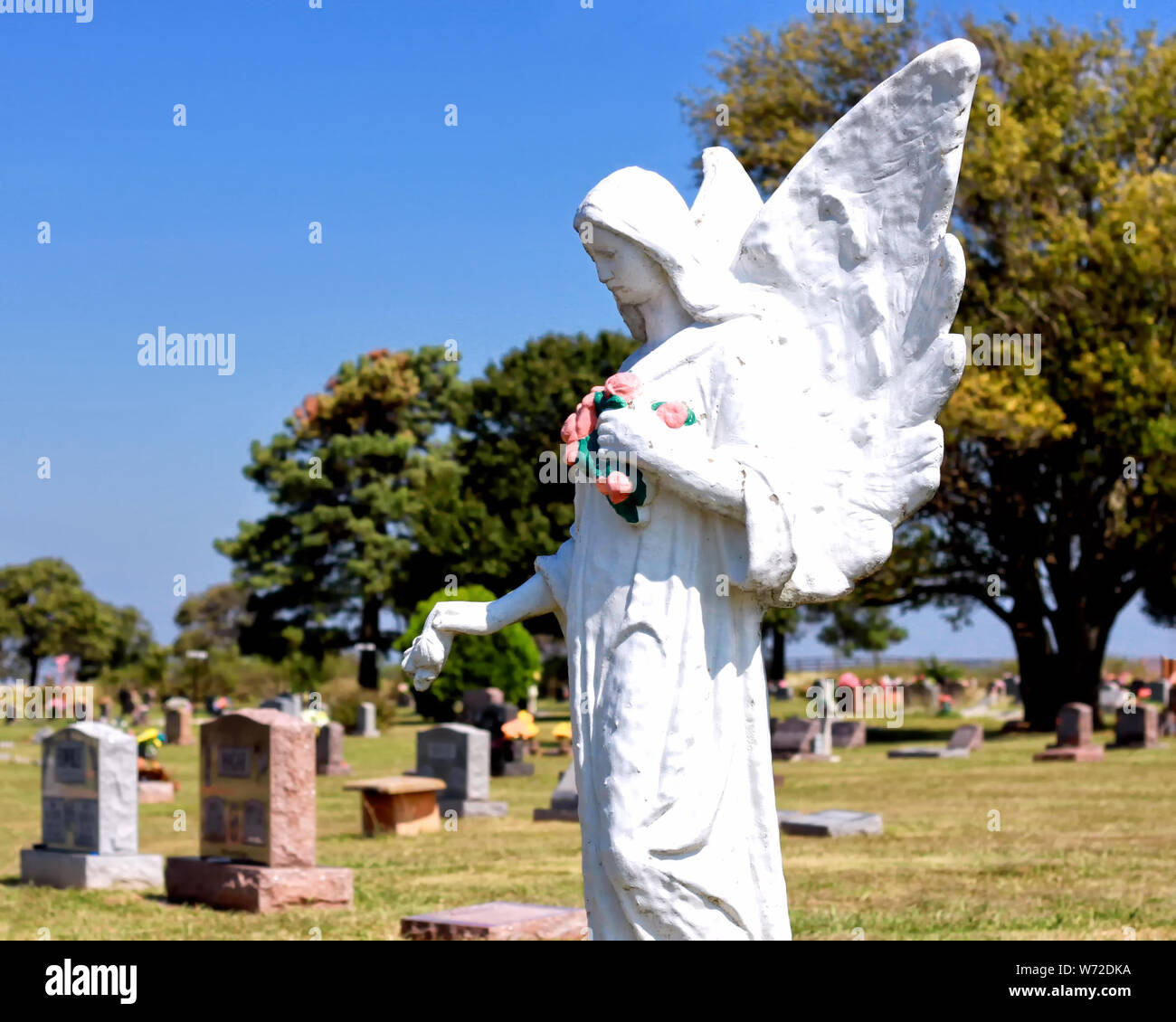 A large white angel statue watches over graves in the Carney Cemetery outside Carney Oklahoma. Stock Photo