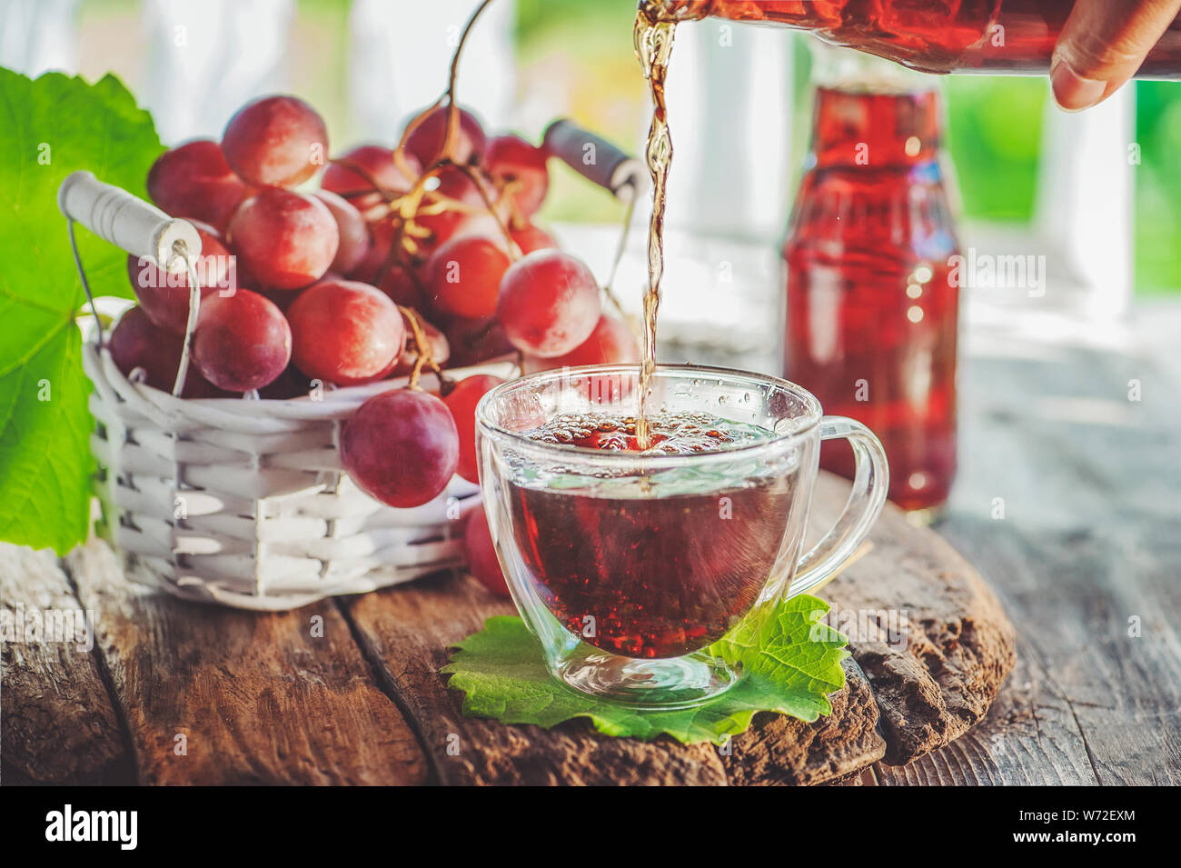 Grape juice pours from the bottle into a glass Cup. Bunch of grapes in