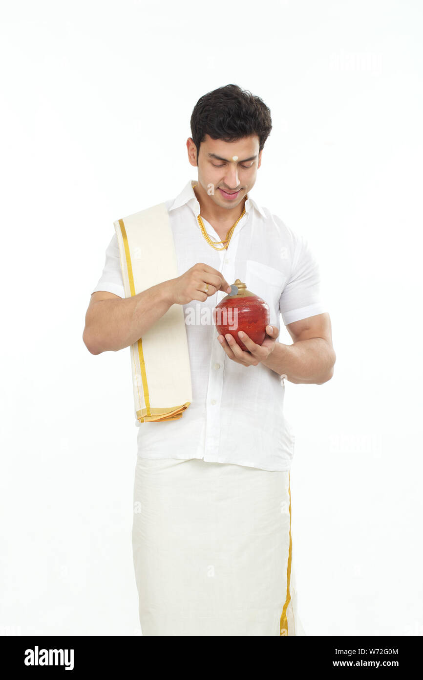 South Indian man inserting a coin into a piggy bank Stock Photo - Alamy