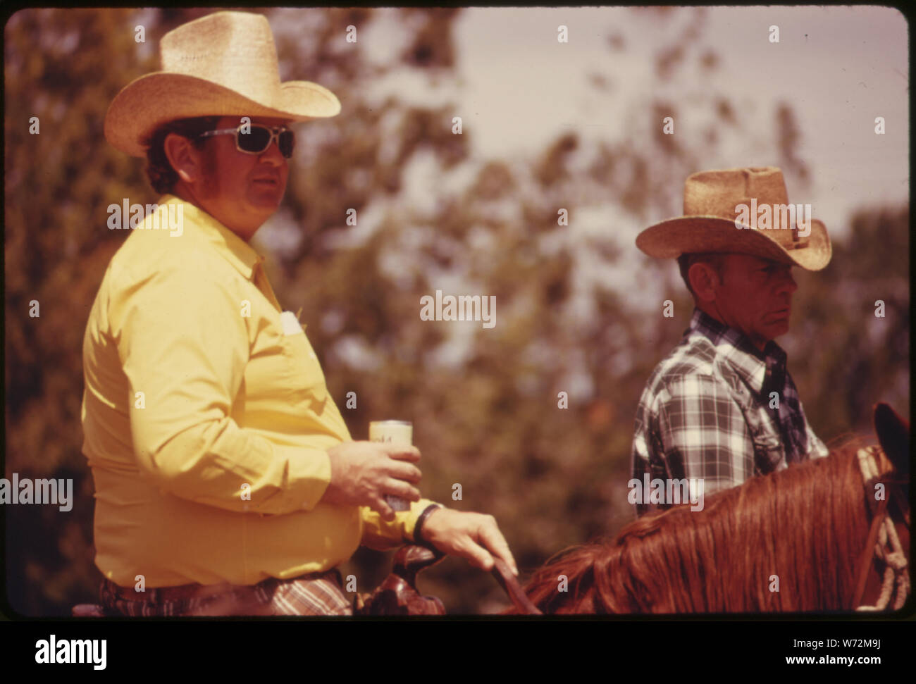 MOUNTED HORSEMEN, ONE RELAXING WITH A CAN OF BEER, AWAIT THE START OF THE PARADE IN COTTONWOOD