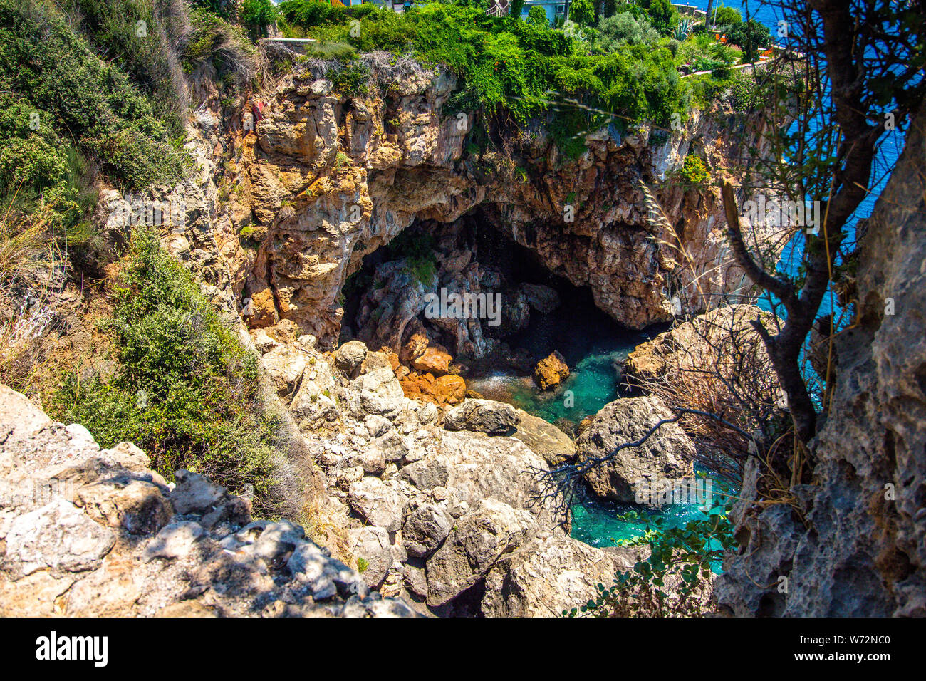 Top view of the rock and blue sea water. In the rock there is a large cave which is flooded with sea water. Stock Photo