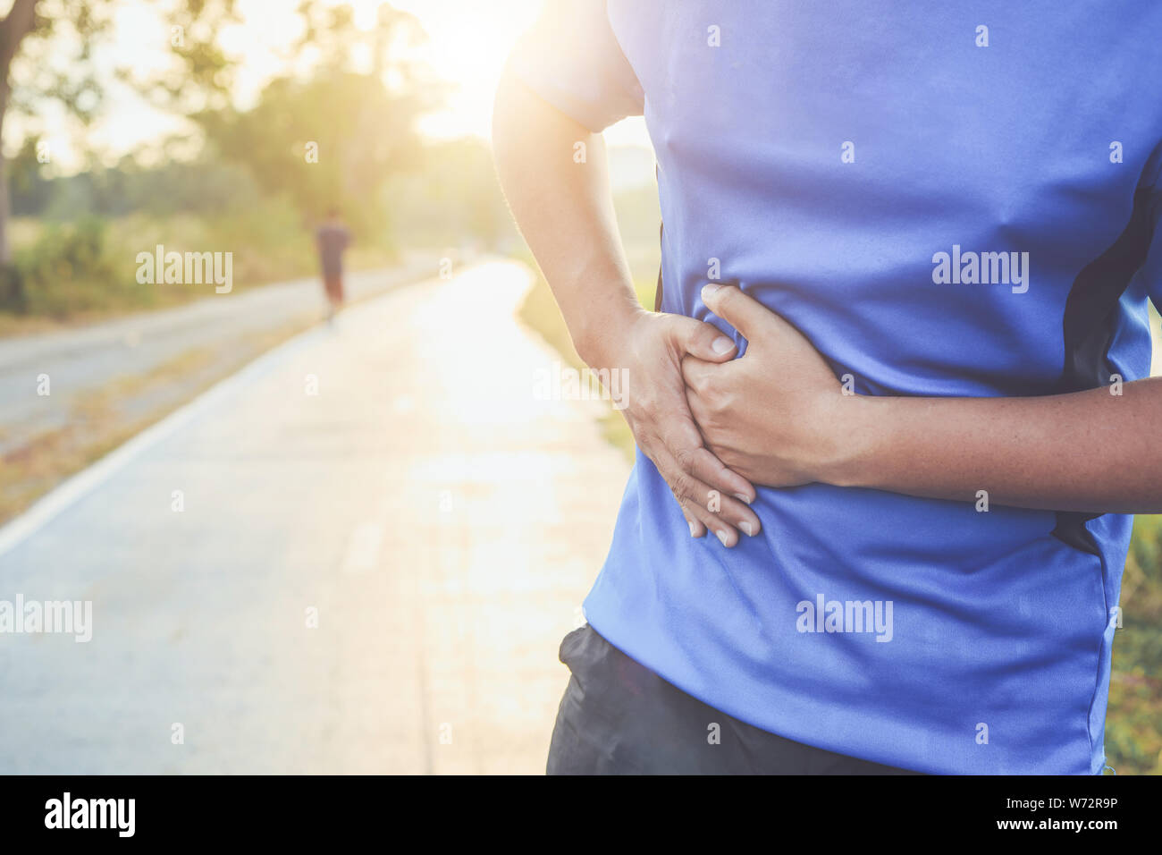 Stomach cramps or Injury while workout concept : The asian man use hands hold on his stomach while running on road in the park Stock Photo