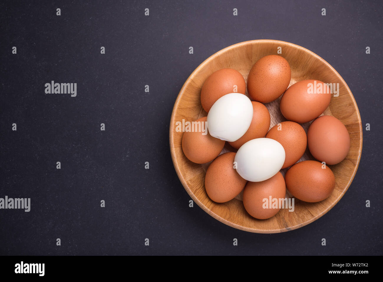 Fresh egg and boiled egg without shell. Top view on black stone