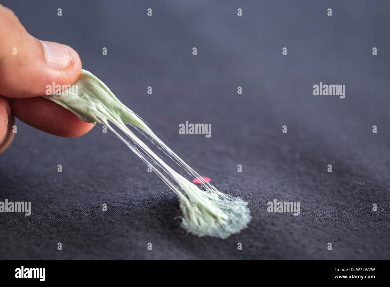 Close up hand removing sticky chewing gum from black textile or clothes Stock Photo