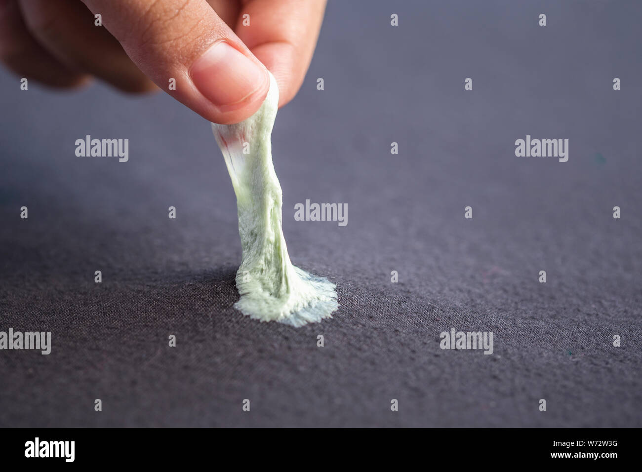 Close up hand removing sticky chewing gum from black textile or clothes Stock Photo