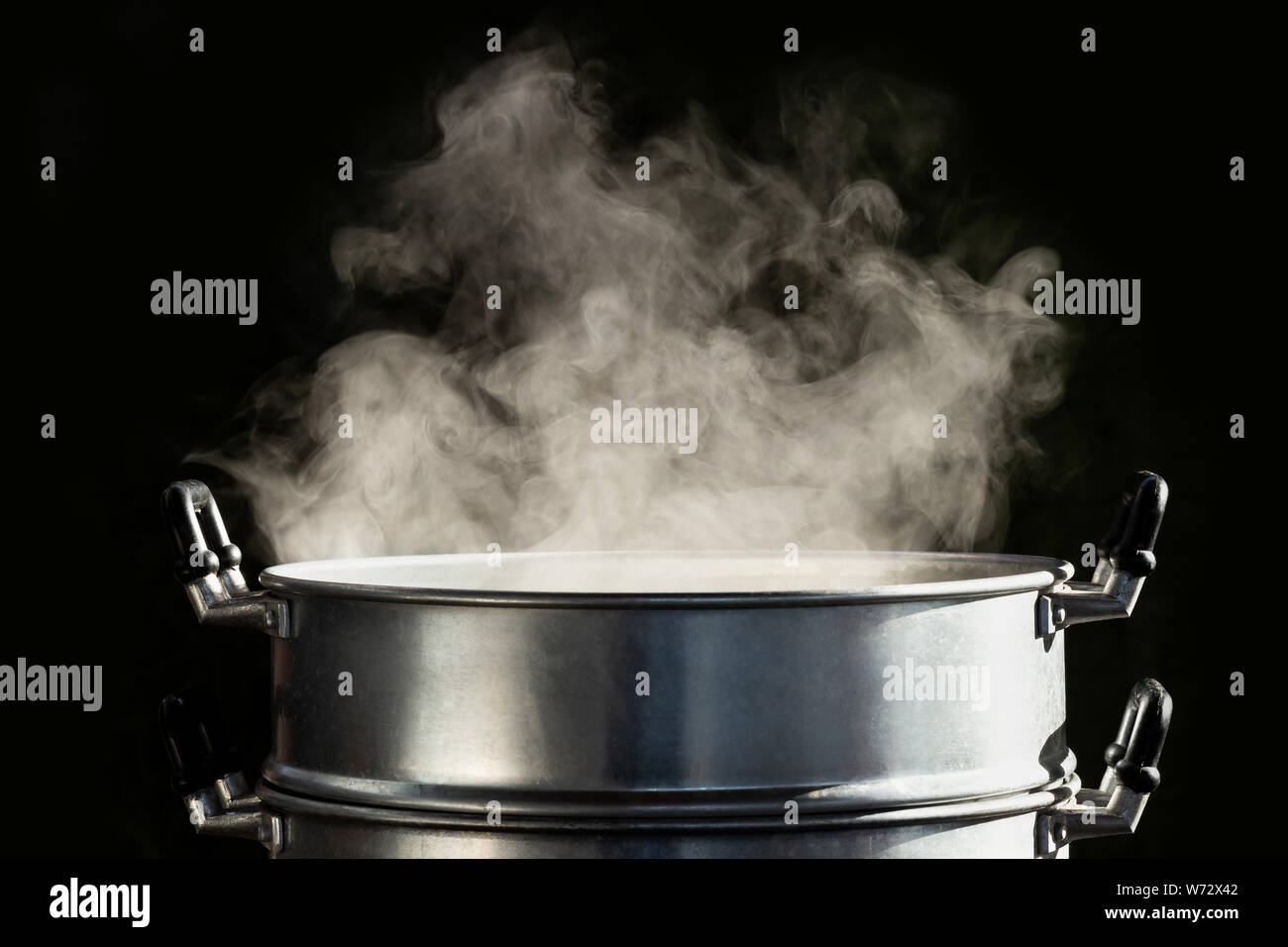Traditional silver steamer pot with white smoke while cooking on black background Stock Photo
