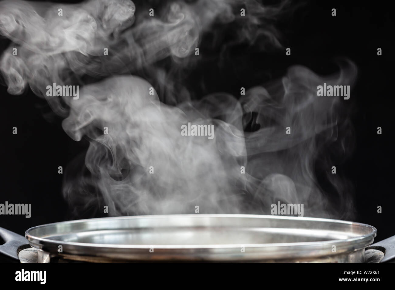 Traditional silver cooking pot with white smoke while cooking on black background Stock Photo