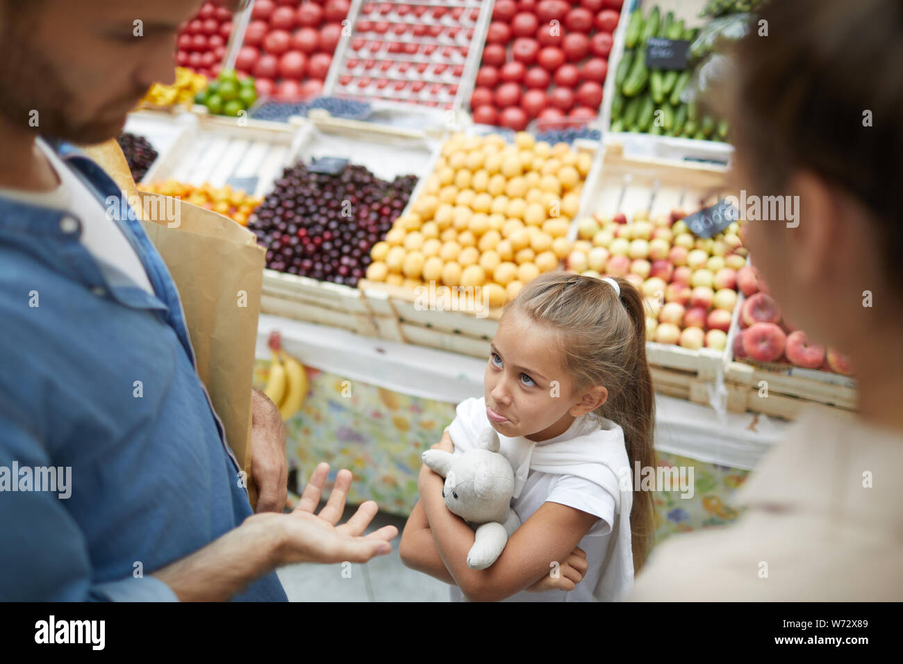 High angle view at spoiled little girl refusing to cooperate with parents at farmers market, copy space Stock Photo