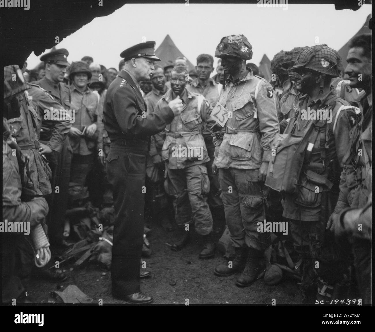 Photograph of General Dwight D. Eisenhower Meeting the Troops Prior to the Normandy Invasion; Scope and content:  Original Caption: General Dwight D. Eisenhower meets with U.S. paratroopers in England, just before they board their airplanes to participate in the first assault in the invasion of the continent of Europe, the Normandy Invasion. Stock Photo