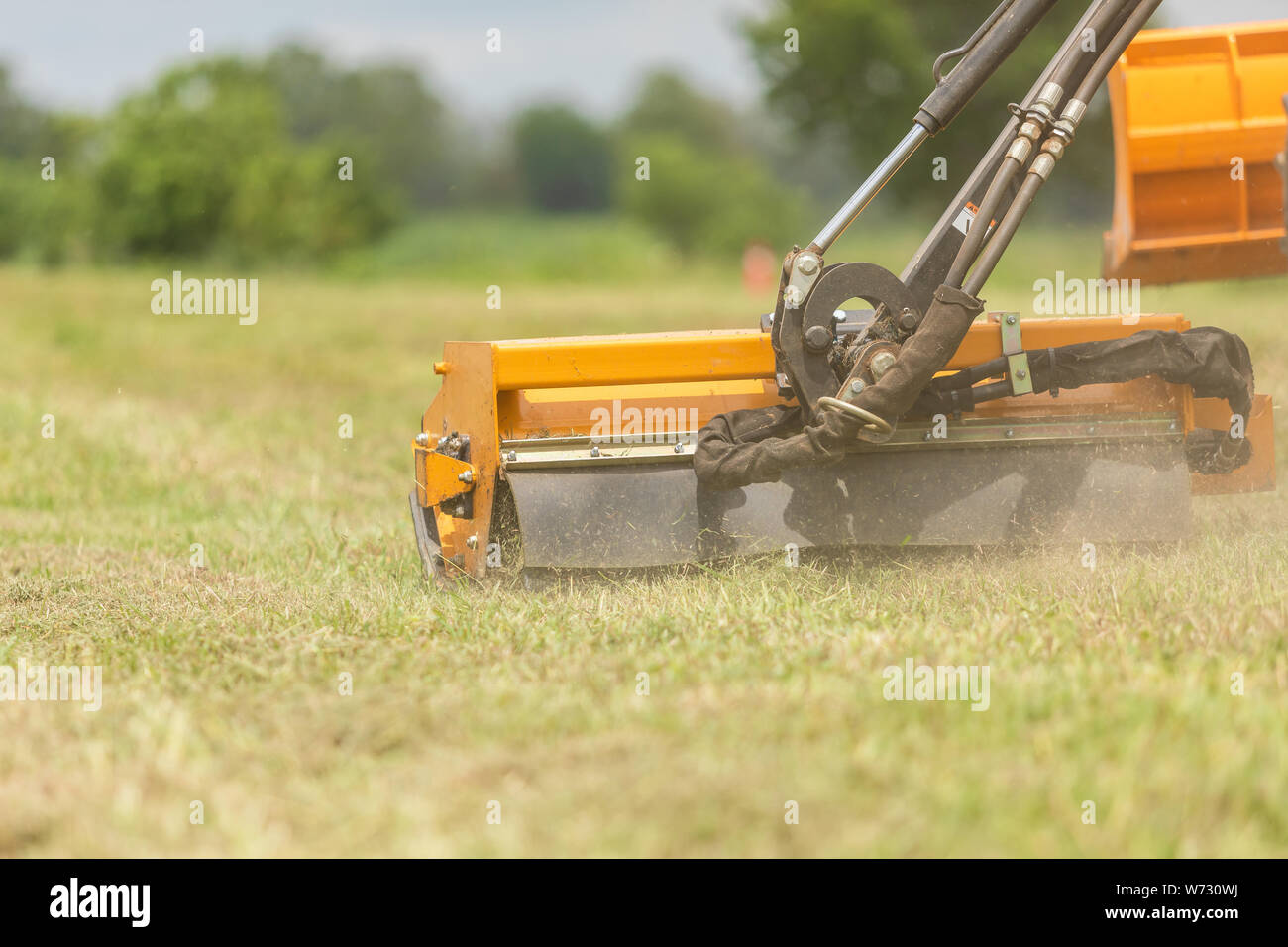 Tractor with a mechanical mower mowing grass on the side of the asphalt road. Working outdoor concept Stock Photo
