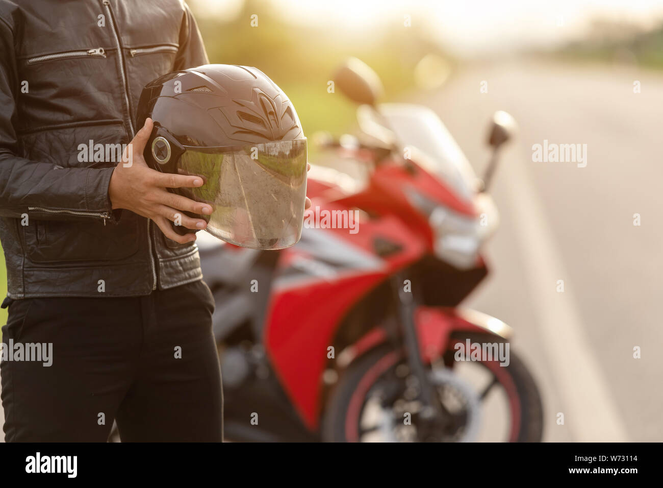 Handsome motorcyclist wear leather jacket and holding helmet on the