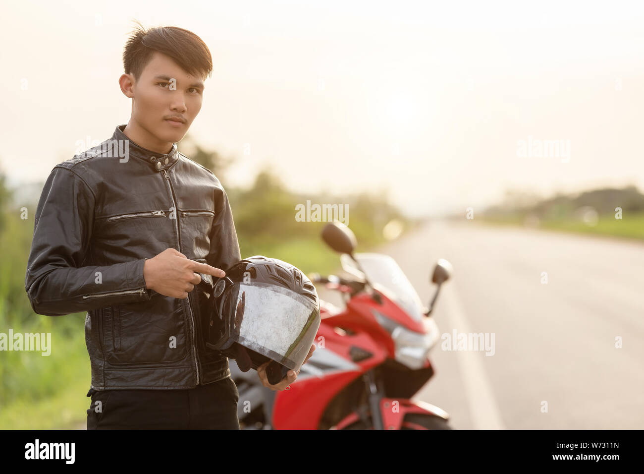 Handsome motorcyclist wear leather jacket and holding helmet on the