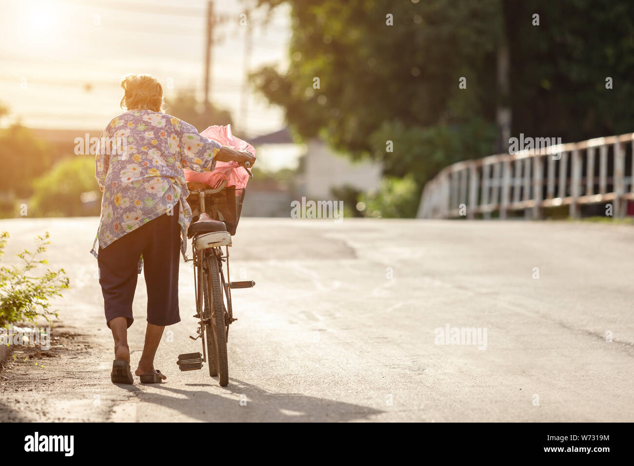 The grandmother walking with old bicycle on the street. Retire but no one take care concept Stock Photo