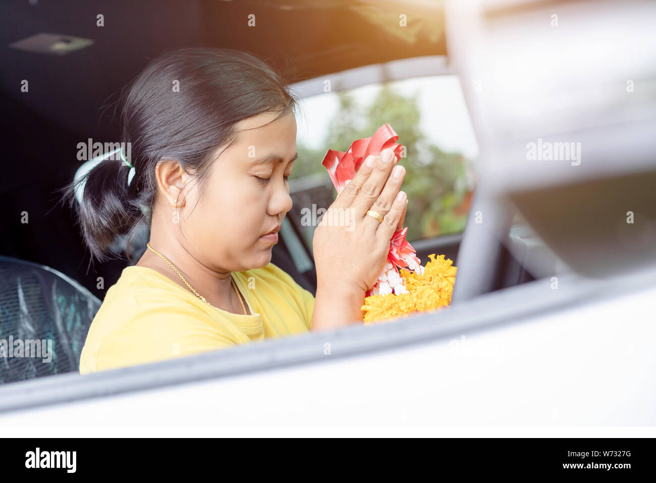 Thai woman with yellow flower garland in hand and praying in the new car for lucky, safety in Thai style Stock Photo