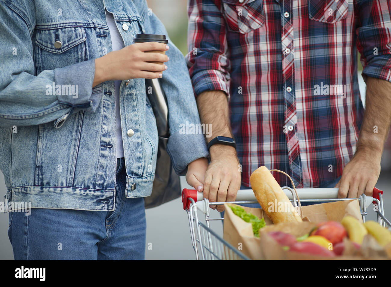 Mid-section portrait of contemporary young couple pushing shopping cart with groceries in parking lot, copy space Stock Photo