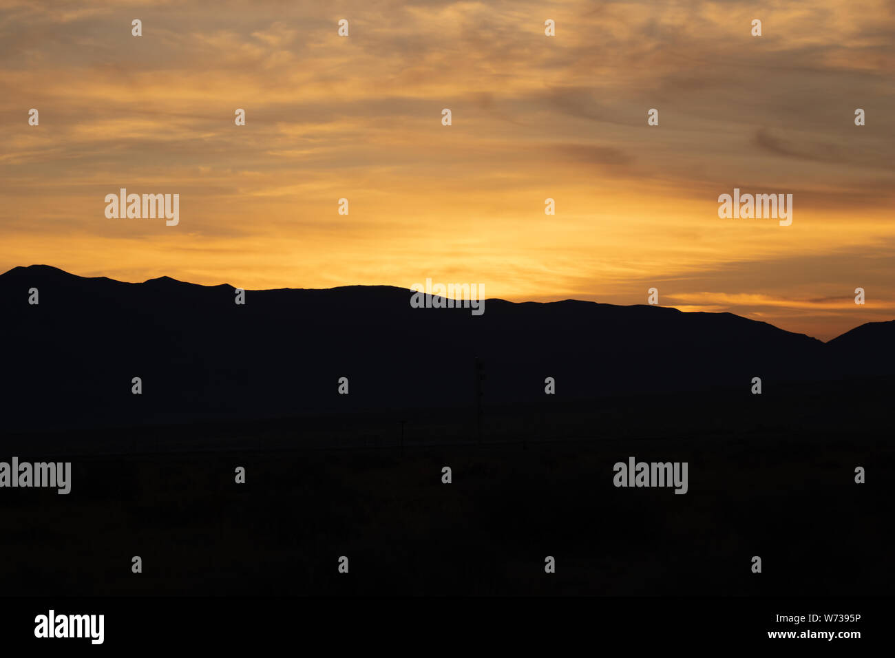 Bright orange sunrise above the silhouette of a mountain in the California desert Stock Photo