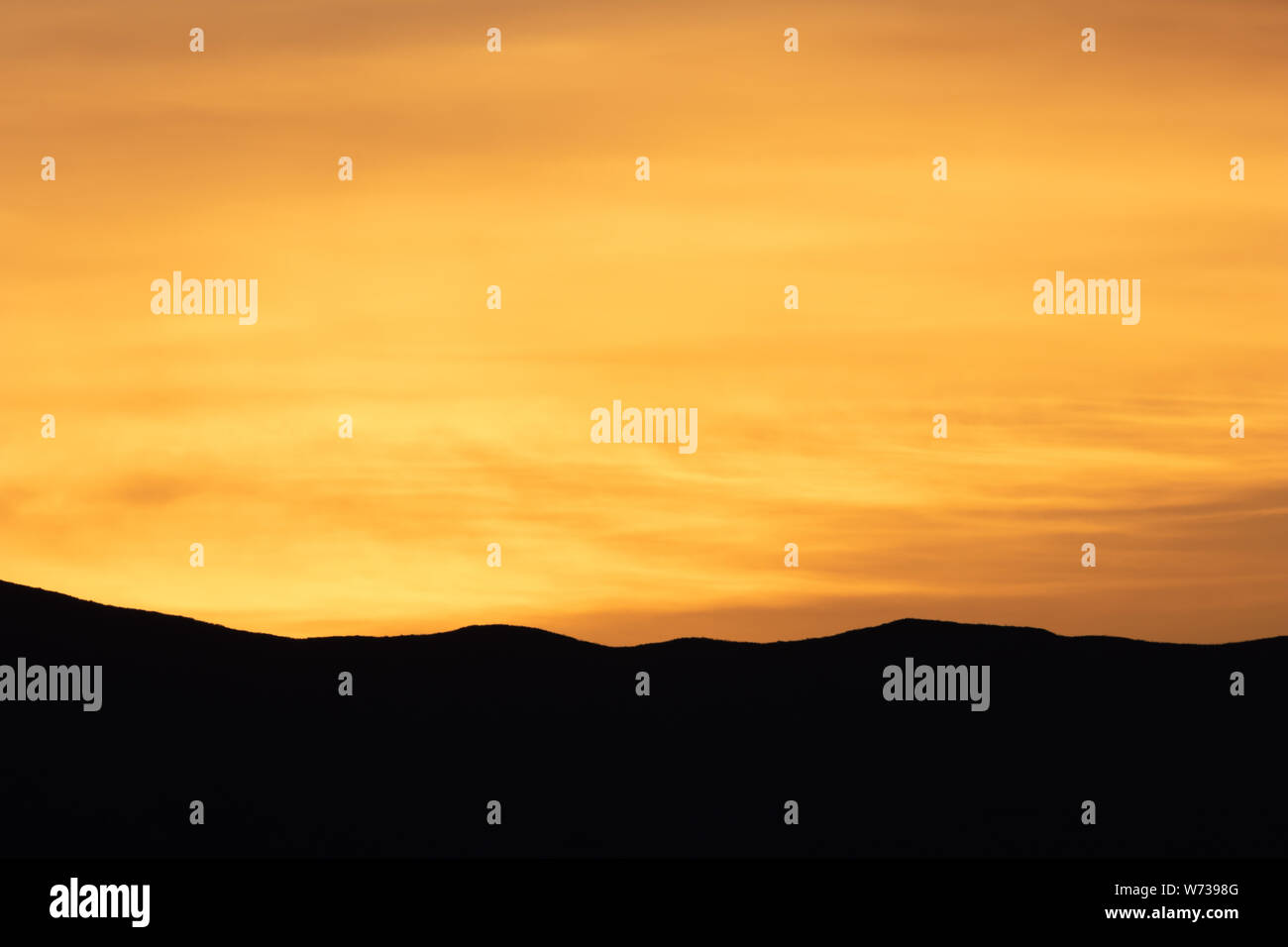 Bright orange sunrise above the silhouette of a mountain in the California desert Stock Photo