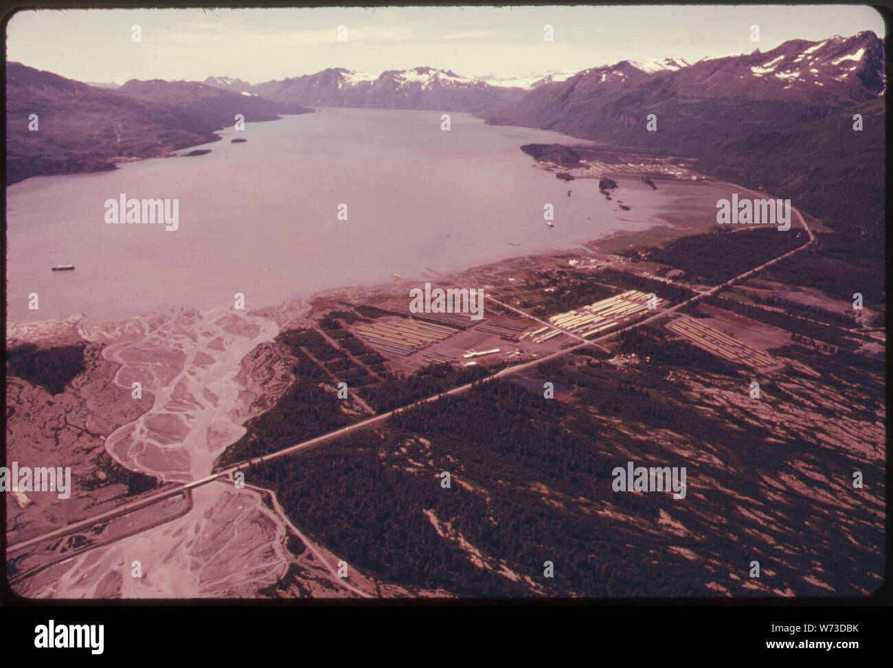 VIEW WEST ALONG PORT VALDEZ. TERMINAL SITE VISIBLE ON HILLSIDE AT CENTER LEFT ABOVE PENINSULA (JACKSON POINT) AND SMALL ISLET (SAW ISLAND). CITY OF VALDEZ (1970 POPULATION 1,000; 1974 POPULATION 2,000) APPEARS AT CENTER RIGHT SOME 418 MILES OF 48-INCH DIAMETER PIPE ARE STORED IN YARDS IN THE LOWER CENTER FOREGROUND. THE RICHARDSON HIGHWAY ARCS ACROSS THE LOWER FOREGROUND TO SWING AROUND THE NORTHEAST END OF PORT VALDEZ TO REACH THE NEW TOWNSITE. MILE 788-789 ALASKA PIPELINE ROUTE Stock Photo