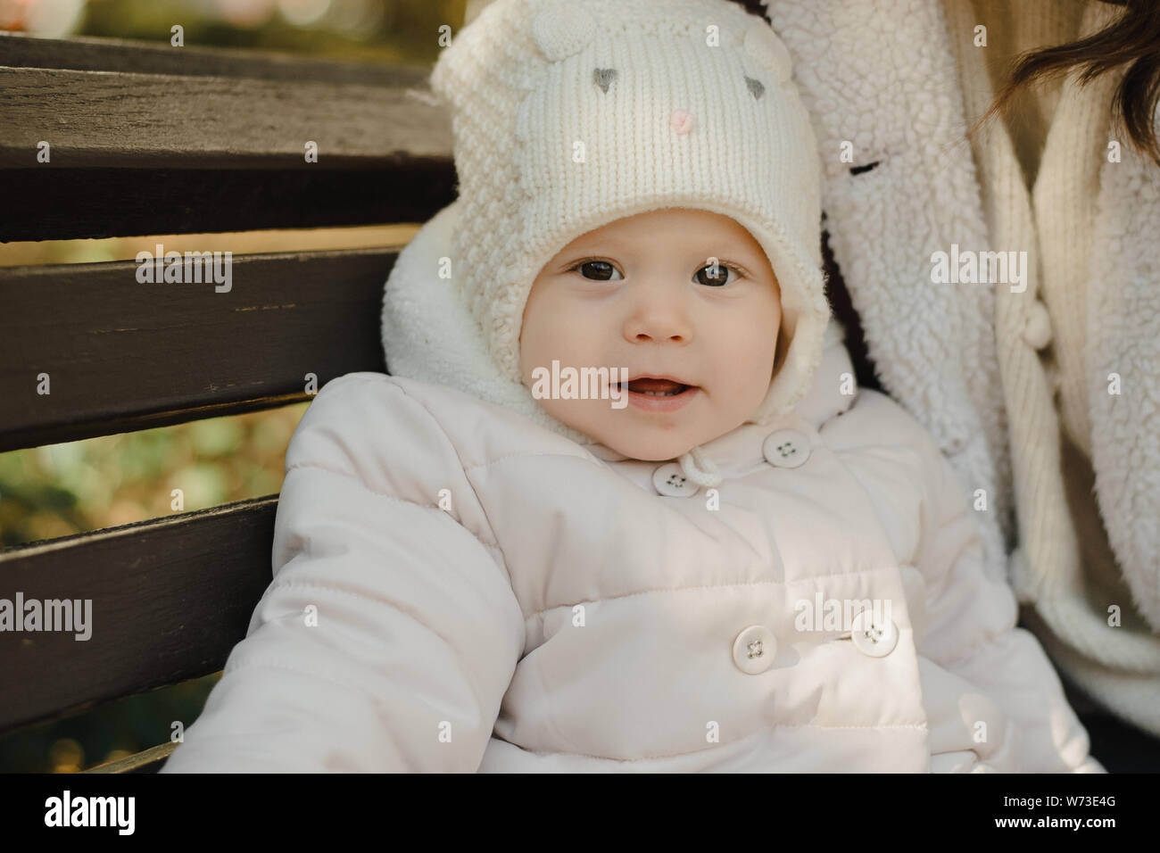 Little Cute Girl Sitting On The Bench The Baby In The Cap And
