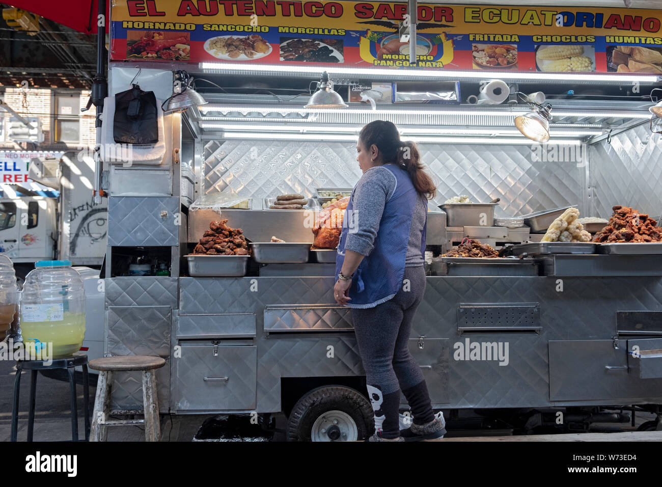 A Hispanic woman selling Ecuadorian food from a cart under the elevated subway on Roosevelt Avenue on Corona, Queens, New York City. Stock Photo