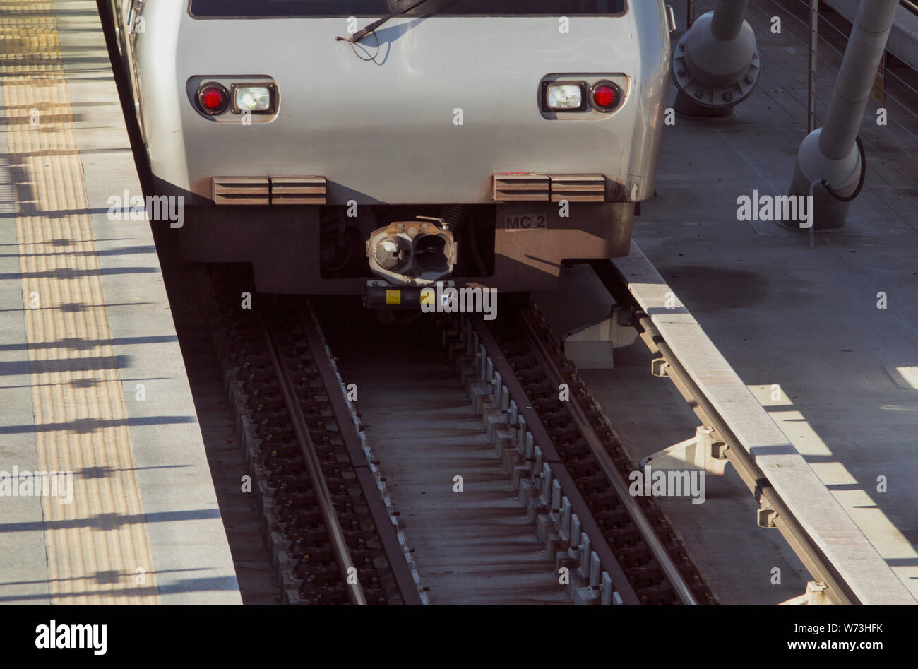Section of a metro train seen from front next to an empty passenger platform on a suspension bridge in daylight. Stock Photo